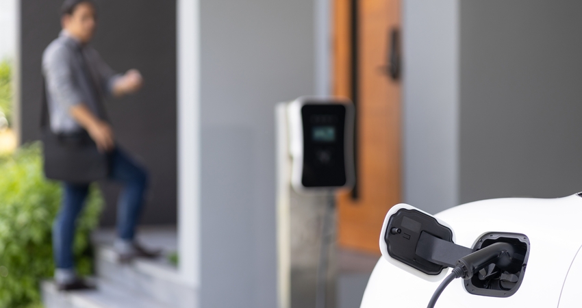 A white electric vehicle plugged into an EV home charger outside a modern house.