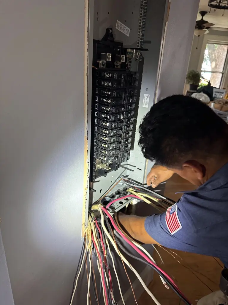 Electrician working on residential electrical panel with circuit breakers and wiring