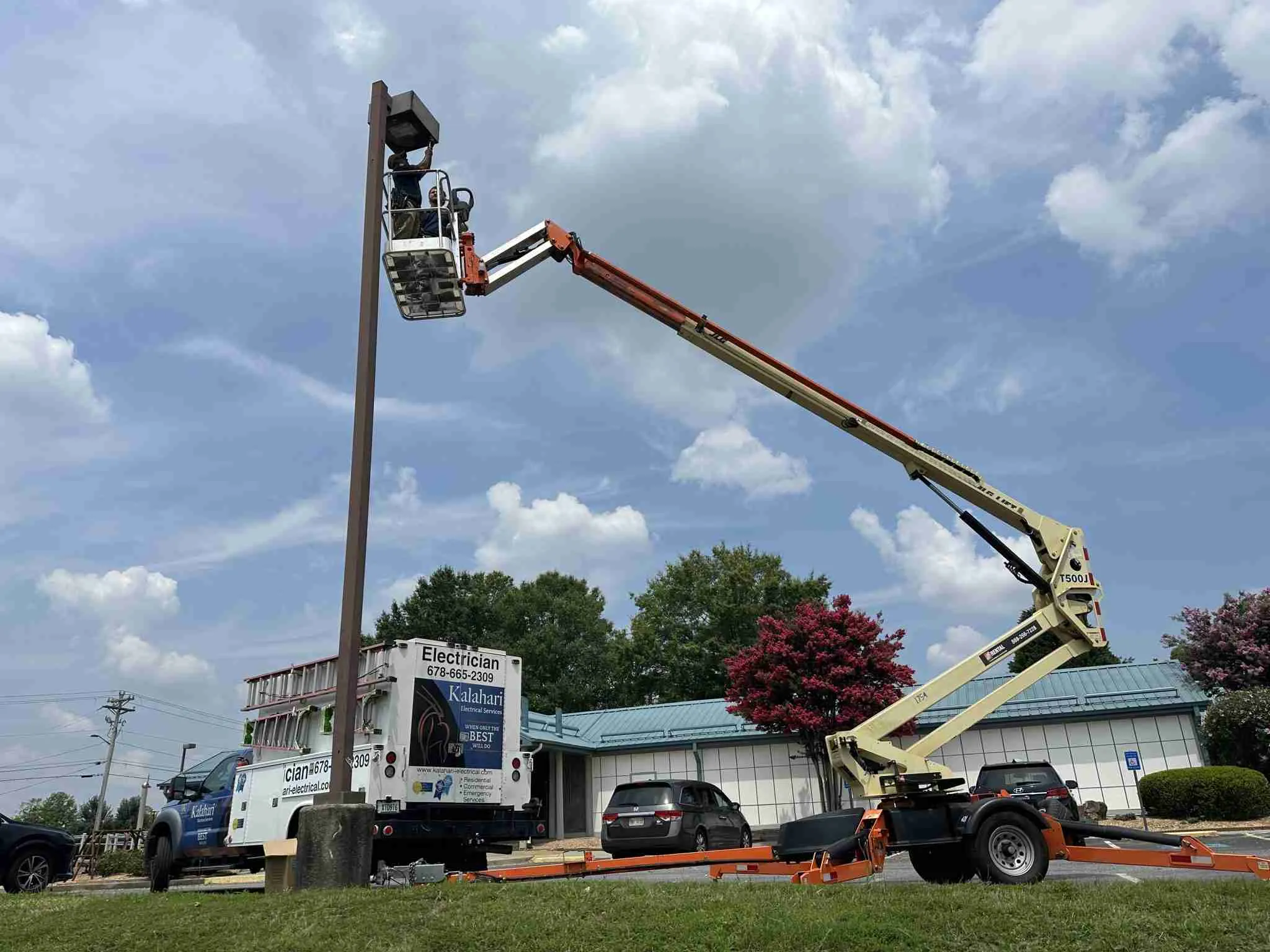 Electrician on boom lift working on tall outdoor light fixture with Kalahari Electrical Services truck below