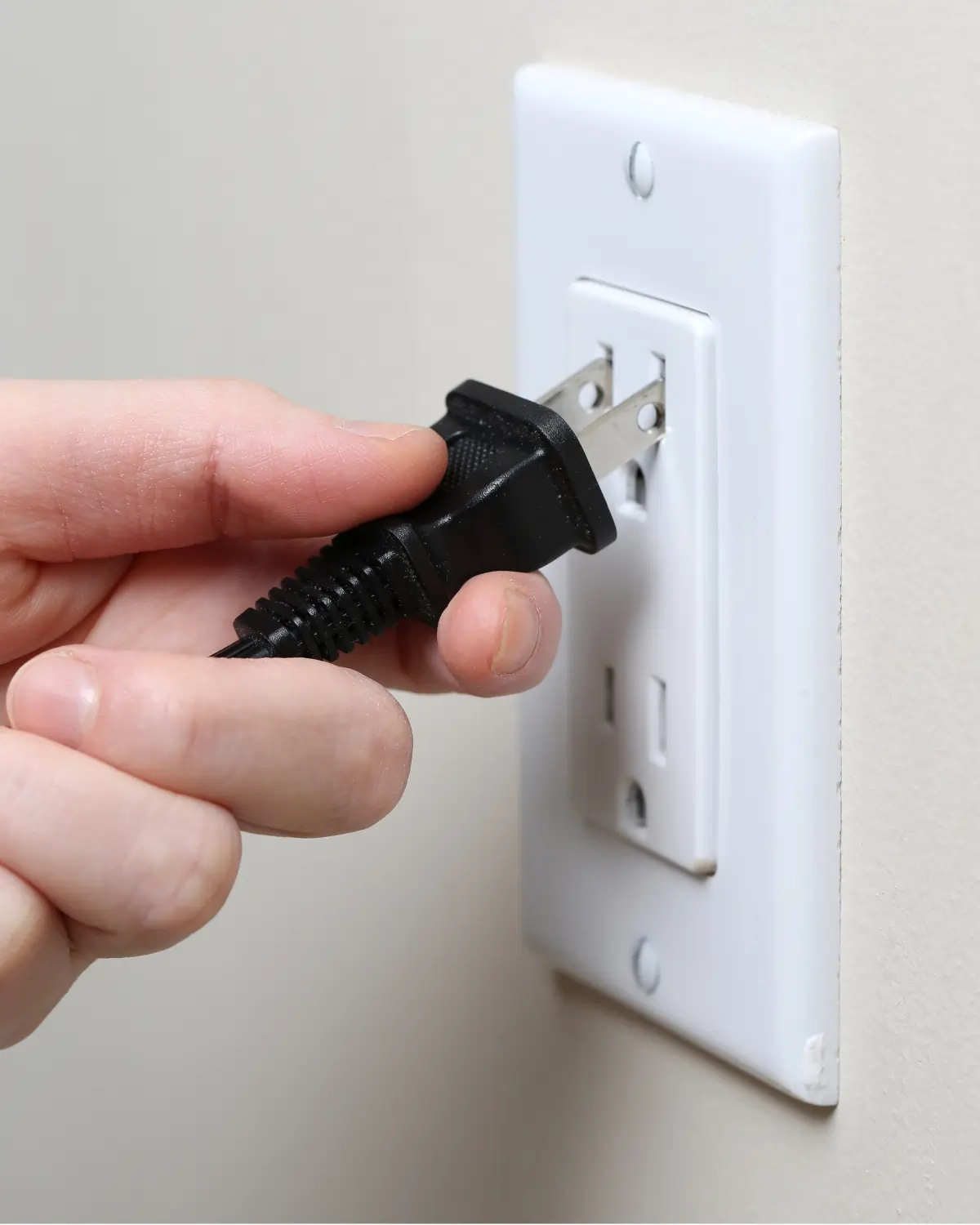 Close-up of plugging electrical cord into wall outlet representing everyday electrical usage